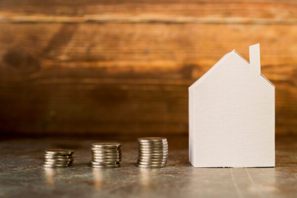 White house-shaped model next to stacked coins on a wooden surface, representing investing in private mortgages