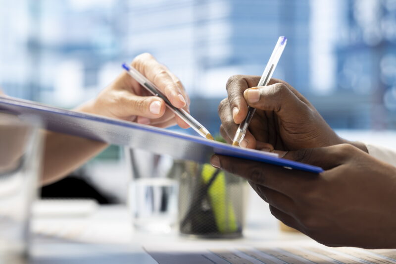 Close-up of two people signing real estate or mortgage documents on a clipboard during a property appraisal meeting.